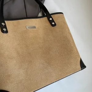 Detail of camel suede tote bag showing black leather trim and silver metal brand logo