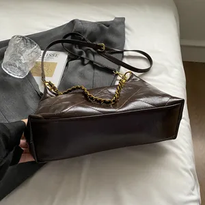 Close-up of dark brown quilted leather bag with gold chain on a minimalist background