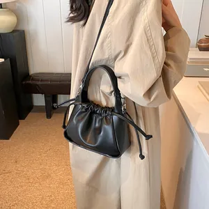 Detail of a black cloud drawstring crossbody bag worn with a classic beige trench coat