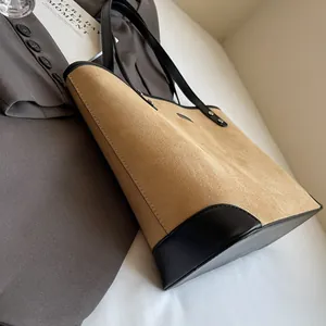 Detail of tan suede tote bag with black leather straps on grey blazer background