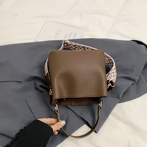 Detail of brown bucket bag with lychee texture and geometric woven shoulder strap
