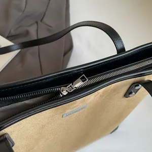 Detailed close-up of khaki suede tote bag featuring silver metal logo and smooth zipper