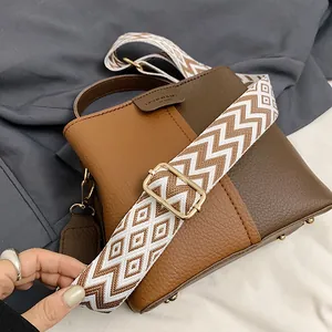 Detailed close-up of textured leather bucket bag with a geometric woven shoulder strap