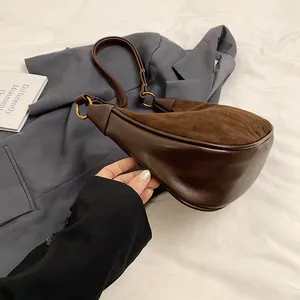 Détail d'un sac à bandoulière marron en demi-lune avec texture daim et anneau doré