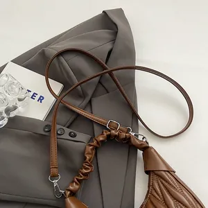 Detailed close-up of brown pleated crossbody bag with V-shaped quilting and silver buckle
