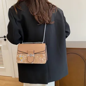 Model wearing a retro khaki crossbody bag with vintage floral patterns and chain strap