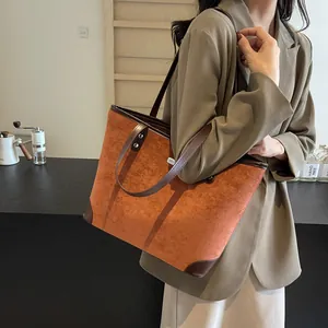 Detail of orange suede tote bag with brown leather straps worn on shoulder