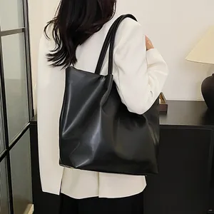Close-up of a large black leather tote bag worn by a model in a minimalist setting