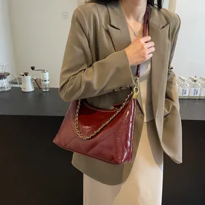 Close-up of wine red quilted shoulder bag with shiny finish and gold chain detail