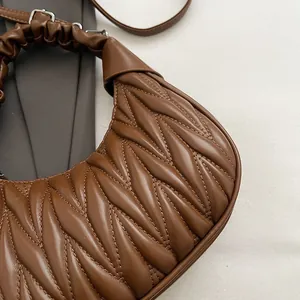 Detail of brown pleated PU leather crescent bag with cloud handle and silver metal hardware