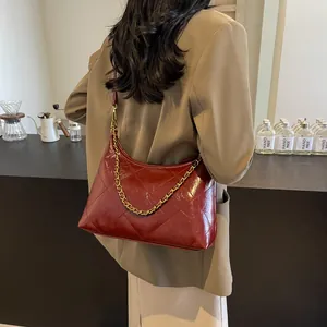 Detail of burgundy quilted leather shoulder bag with gold chain strap on a model