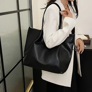 Close-up of a black leather bucket bag with textured pleats on a white suit model