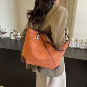Detail of large suede tote bag with brown leather handles and brand metal nameplate
