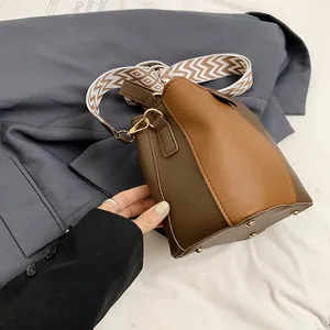 Detail view of contrast leather bucket bag with patterned strap and golden bottom studs