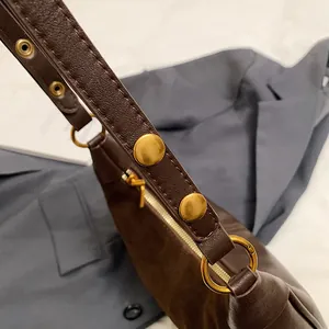 Gros plan sur la bandoulière en cuir marron avec rivets en bronze et zip doré du sac à main
