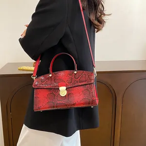 Detailansicht der roten Handtasche mit Schlangenmuster und goldener Schließe am Modell