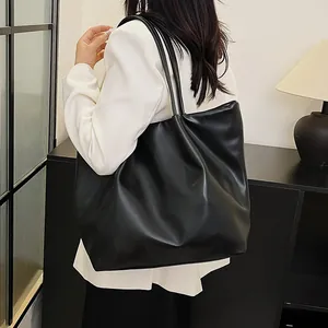 Detailed view of black matte leather large tote bag on model's shoulder in white suit