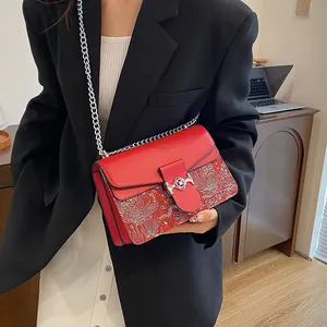 Detail of red leather shoulder bag with white floral embroidery and silver chain strap