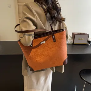 Detail of caramel suede tote bag with brown leather trim and silver metal logo brand