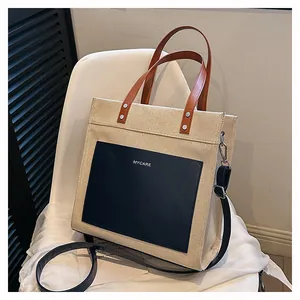 Detail of beige canvas tote bag with black leather pocket and brown handles on chair