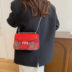 Detail of red crossbody bag featuring silver floral embroidery and a metal chain strap