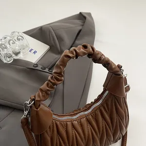 Detailed view of dark brown crescent bag with V-shaped stitching on grey fabric background