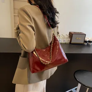 Quilted burgundy shoulder bag with gold chain strap shown on a model in a cozy cafe