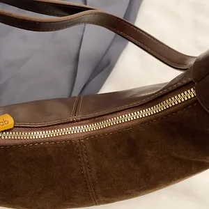 Détail du sac à bandoulière marron foncé en daim et cuir avec fermeture éclair dorée