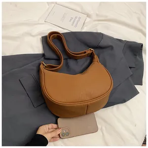 Détail du sac demi-lune en similicuir marron montrant sa capacité à côté d'un smartphone