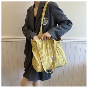 Detail of a bright yellow tote bag with drawstring texture and branded label on model