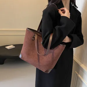 Close-up of brown suede tote bag with leather trim and reinforced corners on black coat