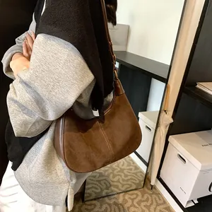 Détail d'un sac hobo en daim marron avec textures mixtes et anneaux métalliques dorés