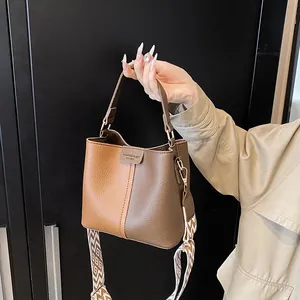 Close-up of brown textured leather bucket bag with patterned wide woven shoulder strap