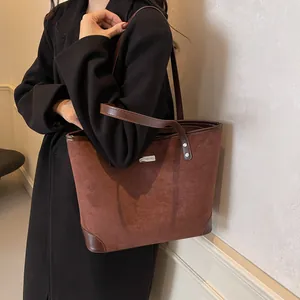 Detail of caramel suede tote bag with brown leather handles worn with a black coat