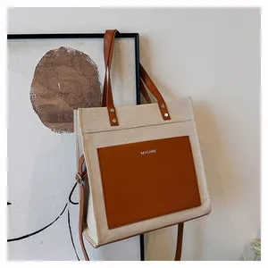 Detail of canvas tote bag with brown leather pocket, dual handles and long strap