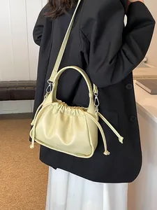 Pale yellow drawstring pleated crossbody bag with a curved handle shown on a model