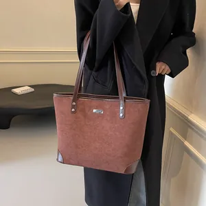 Detail showing the red-brown suede texture and metallic logo plate on the tote bag