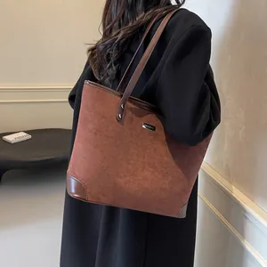 Detailed close-up of brown suede tote bag with leather straps and metal brand logo