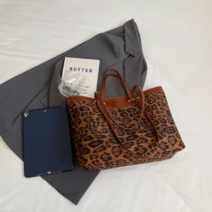 Flat lay of leopard print tote bag with brown leather handles on a grey blazer