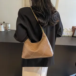 Brown quilted crossbody bag with gold chain strap shown on a shoulder in a cafe setting