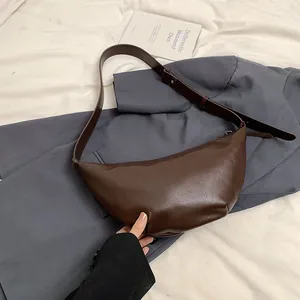 Vista plana de un bolso de media luna marrón oscuro sobre traje gris y tela texturizada