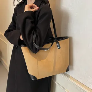 Detail of a large brown suede tote bag with black leather trim and handles shown on a model