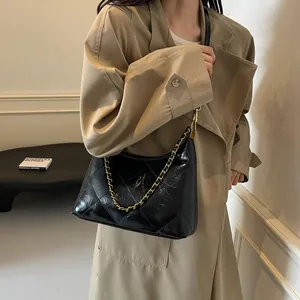 Detail of black quilted patent leather hobo bag with gold chain strap on female model