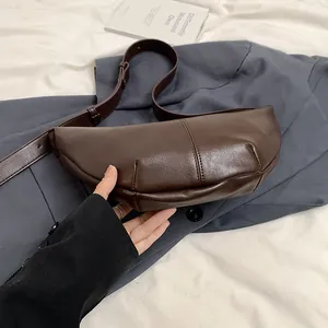 Detalle de bolso medialuna marrón oscuro con correa ajustable sobre traje grisáceo