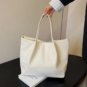 Detail view of cream white PU leather tote bag with soft pleated design on a black table