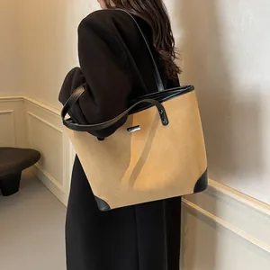 Close-up of brown suede tote bag featuring black leather handles and silver logo plaque