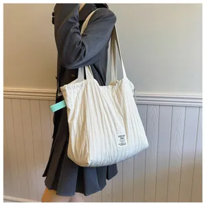 Close-up of white quilted tote bag featuring vertical pleated texture and brand label