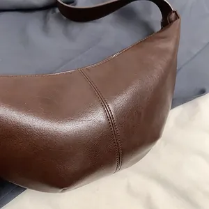Detalle macro del bolso croissant marrón oscuro con costuras y textura de cuero premium