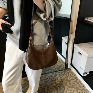 Détail du sac hobo en daim marron foncé avec surpiqûres et anneaux métalliques sur la bandoulière