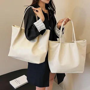 Detail of off-white oversized faux leather tote bags with textured pleats and slim straps